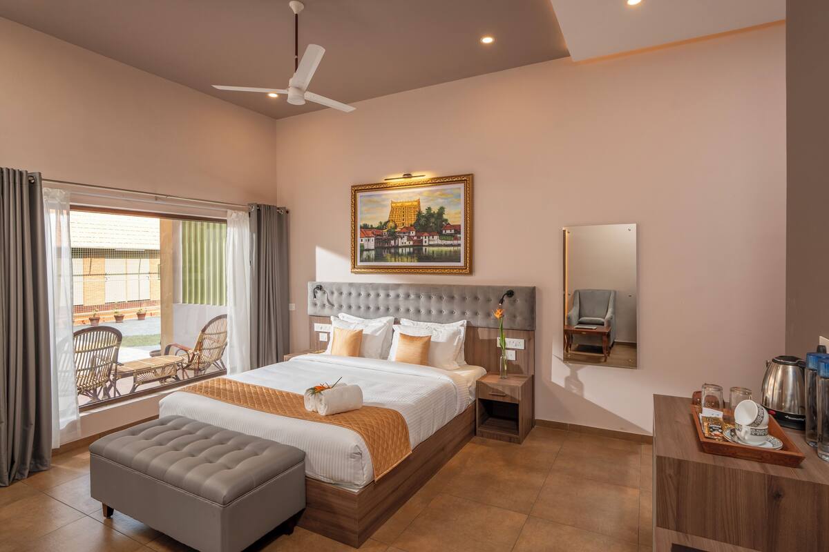 A spacious hotel room with a large bed, a sitting area with chairs, a balcony with a view, and a dining area with a tray of items.
