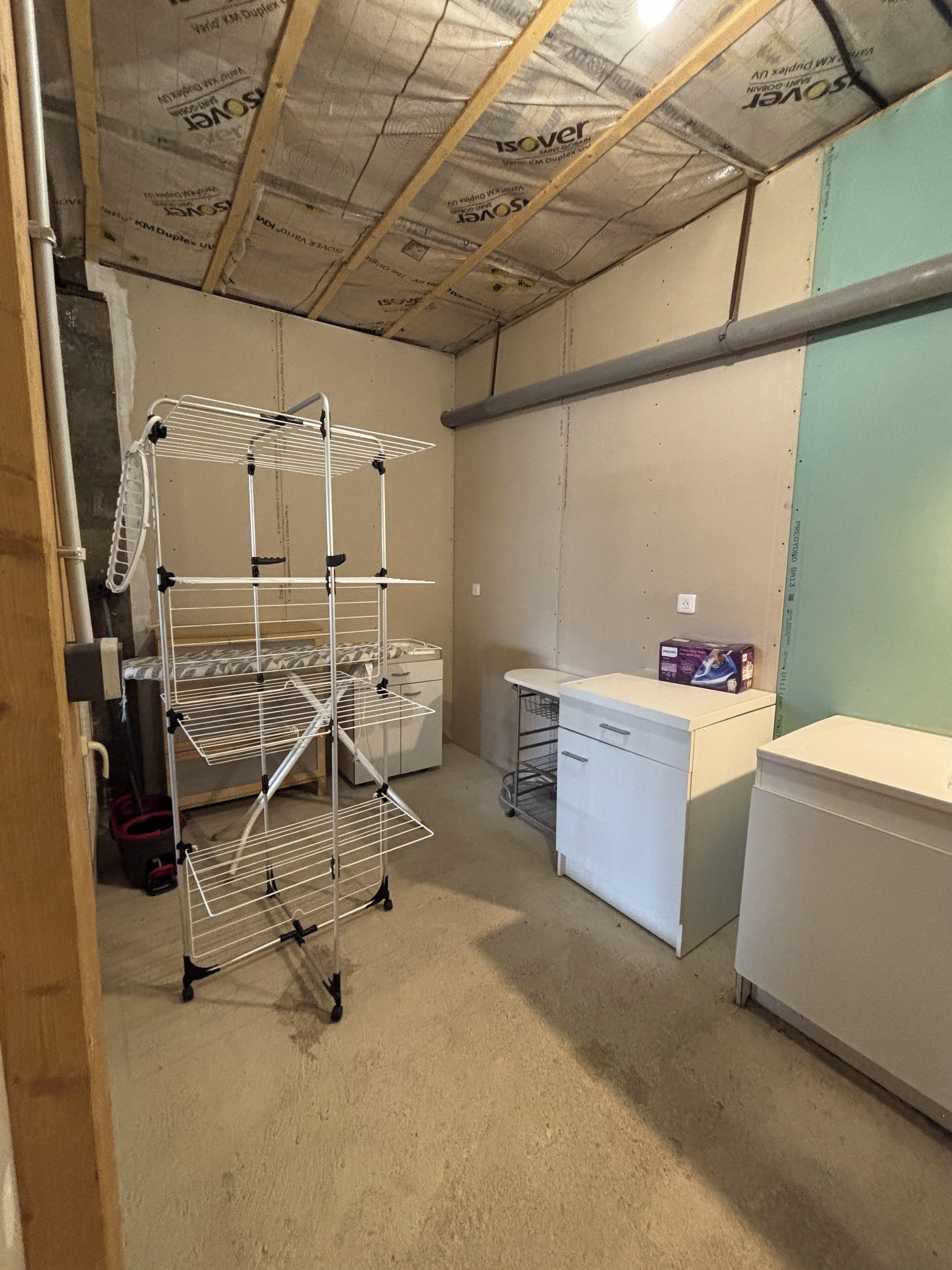 A laundry room with a metal drying rack, a washing machine, and a small table with a box on it.