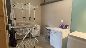 A laundry room with a metal drying rack, a washing machine, and a small table with a box on it.