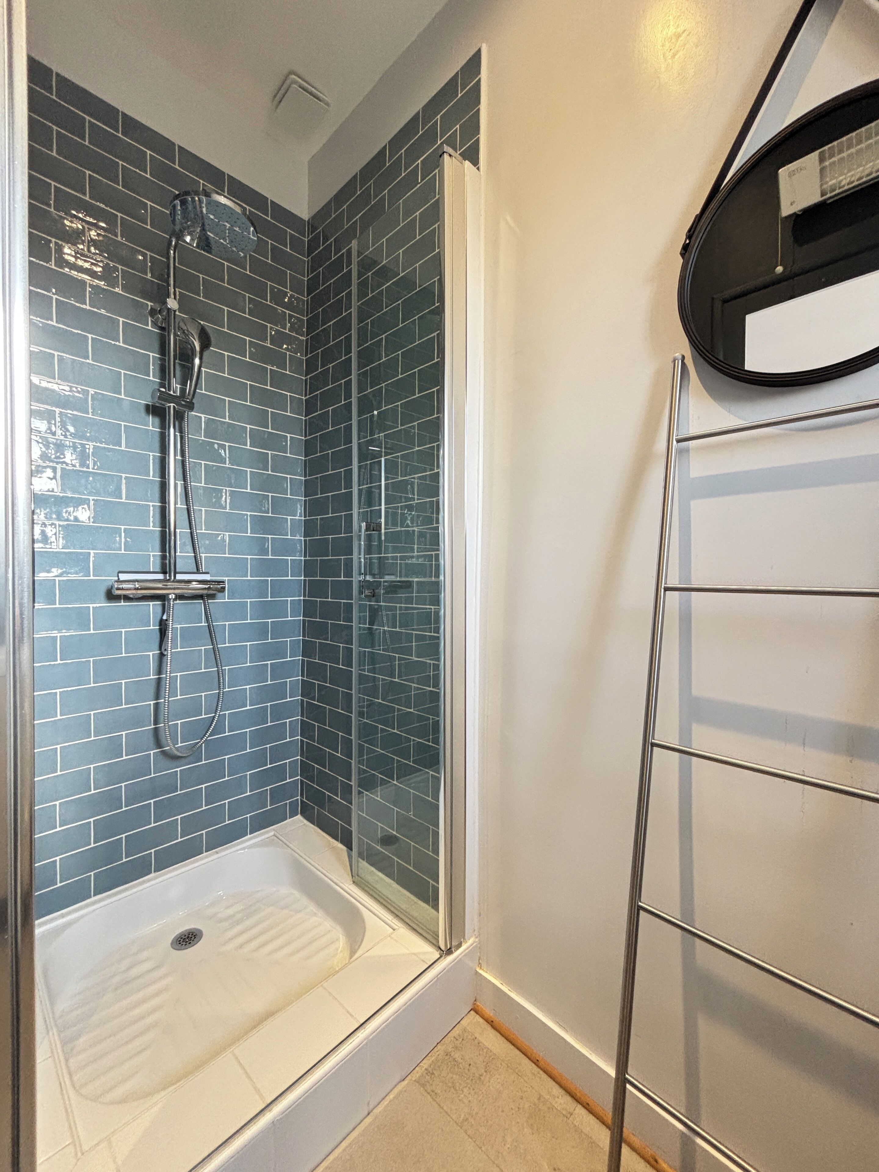 Una ducha con puerta de cristal, un perchero metálico y paredes con azulejos azules.