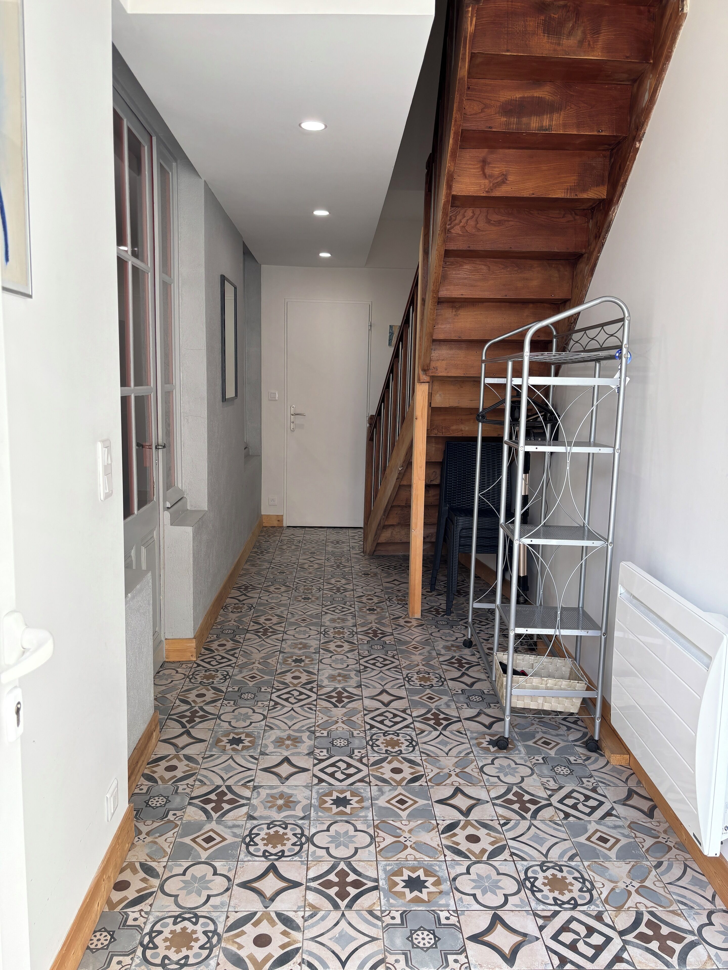A hallway with patterned floor tiles, a wooden staircase, and a metal shelf unit.