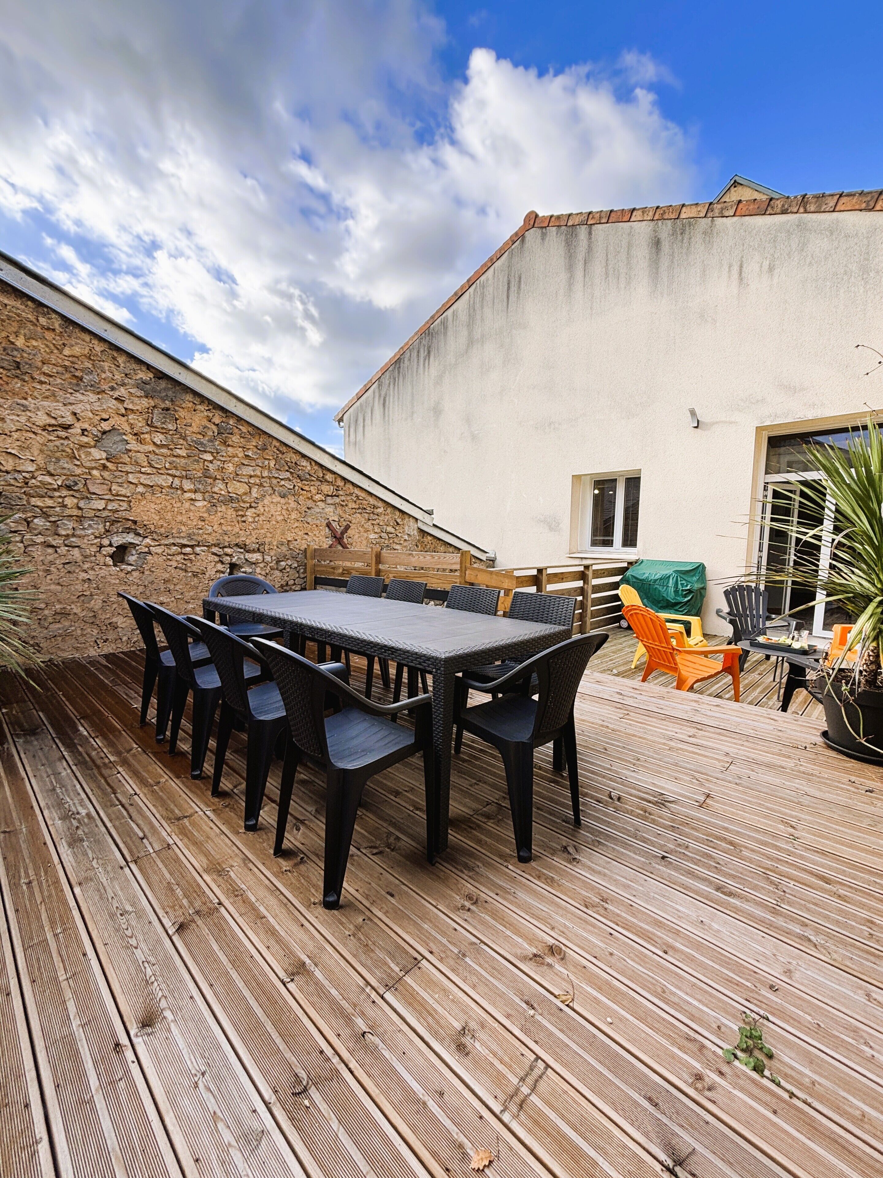 Um pátio externo com deck de madeira, uma mesa com cadeiras e uma parede de pedra.