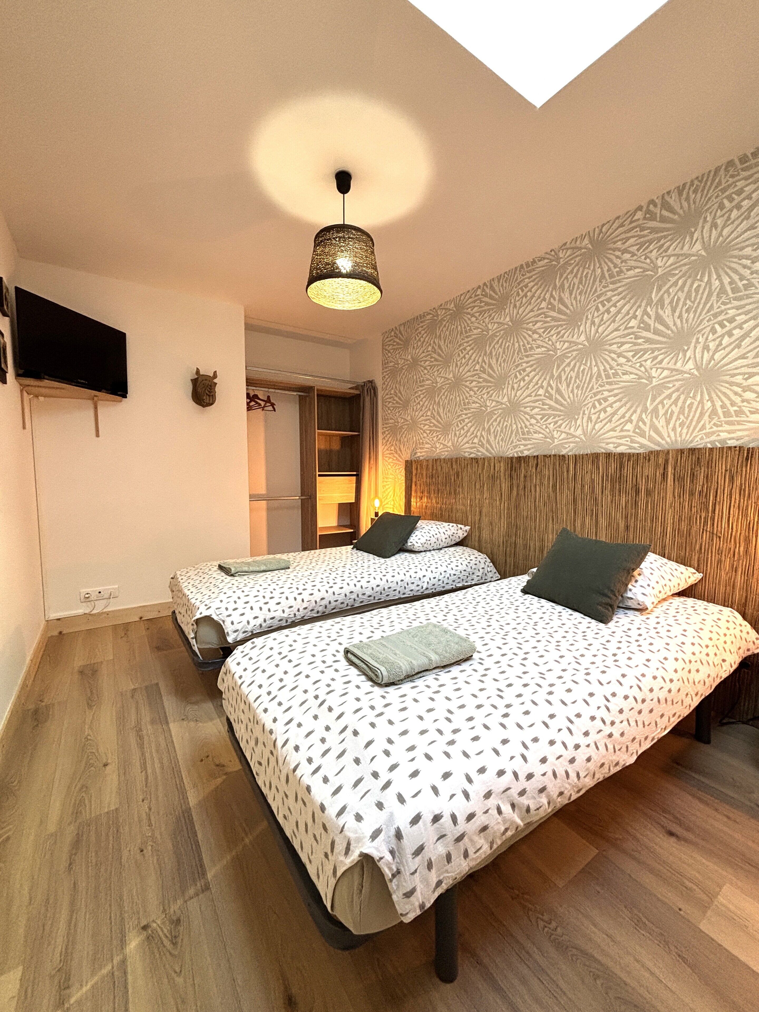 Ein modernes Schlafzimmer mit zwei Betten, einem an der Wand befestigten Fernseher und einem Wanddesign mit Muster.