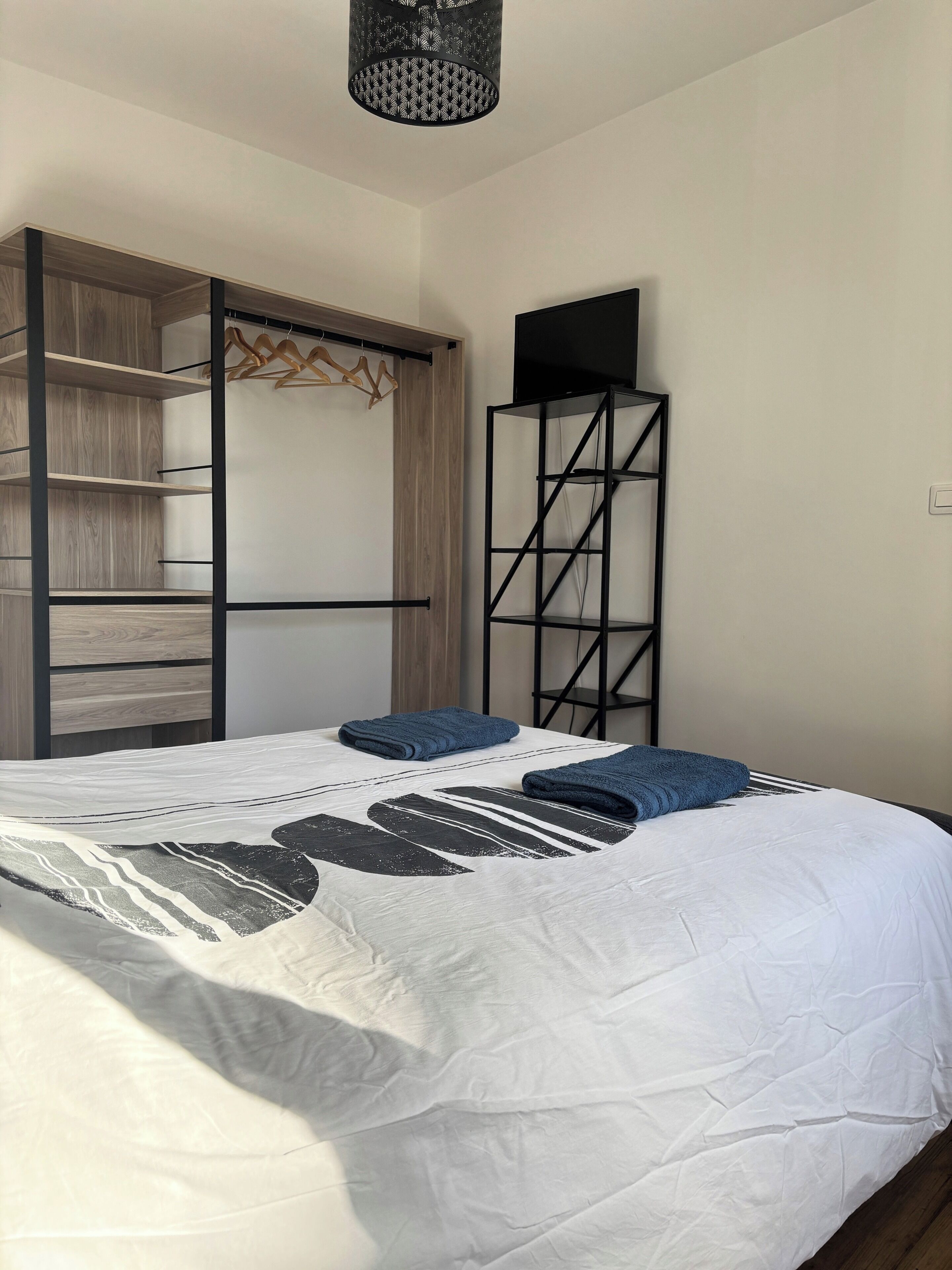 Quarto com cama, guarda-roupa, televisão sobre um suporte e um cabideiro.