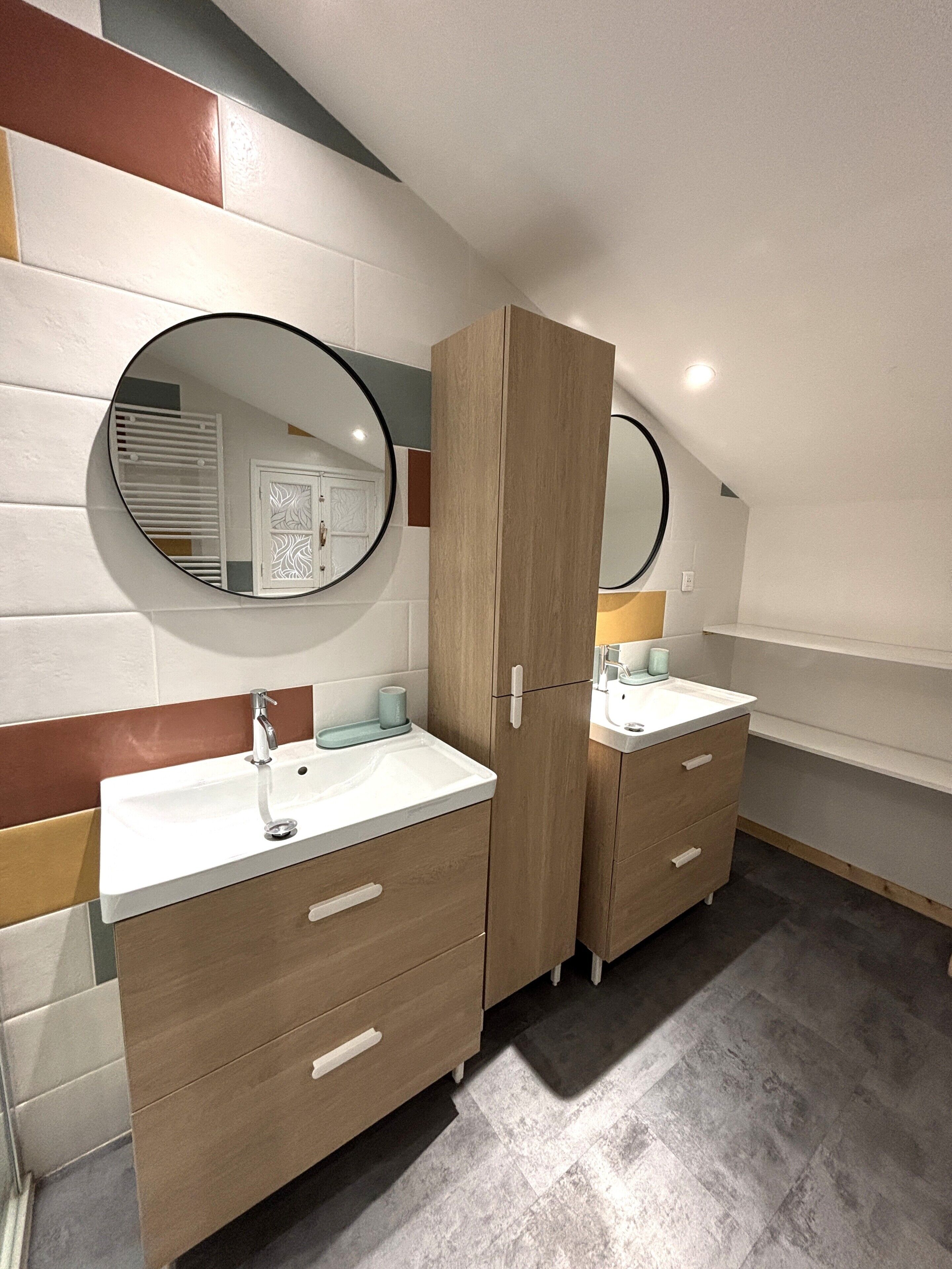 A modern bathroom with two sinks, wooden cabinets, and a large mirror.