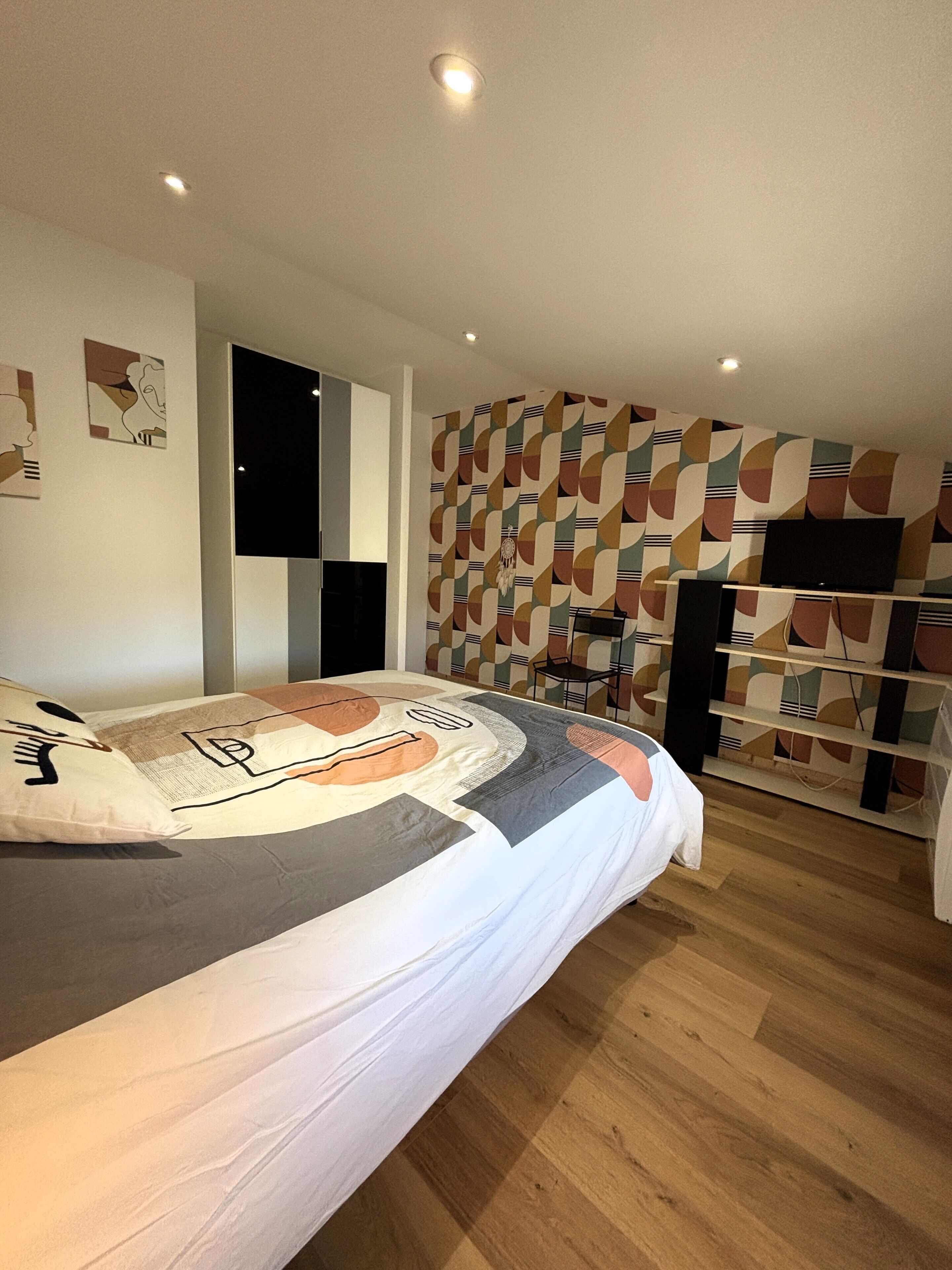 A bedroom with a bed, a television, and a patterned wall.