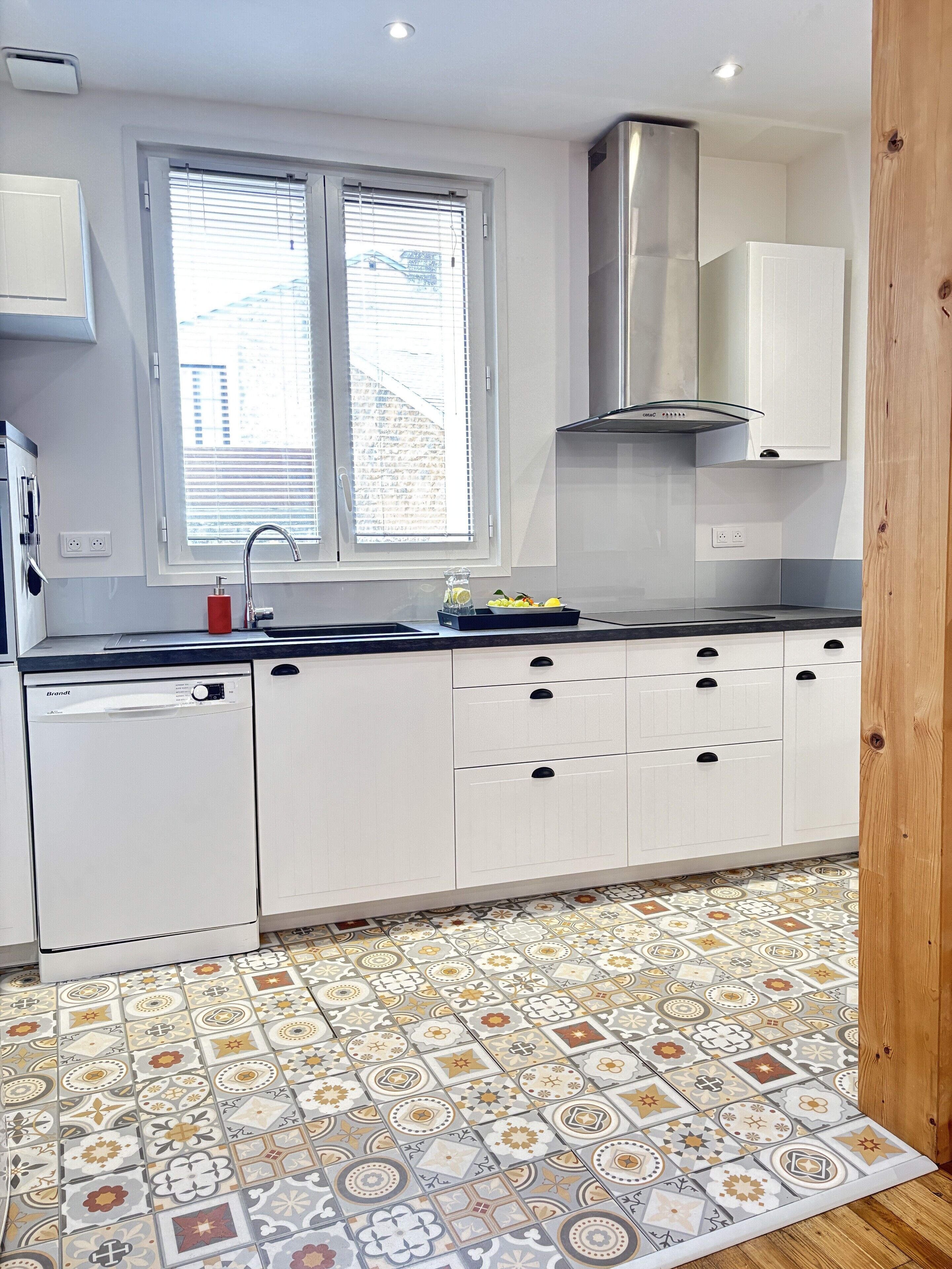 A modern kitchen with white cabinets, a stainless steel range hood, and a window with blinds.