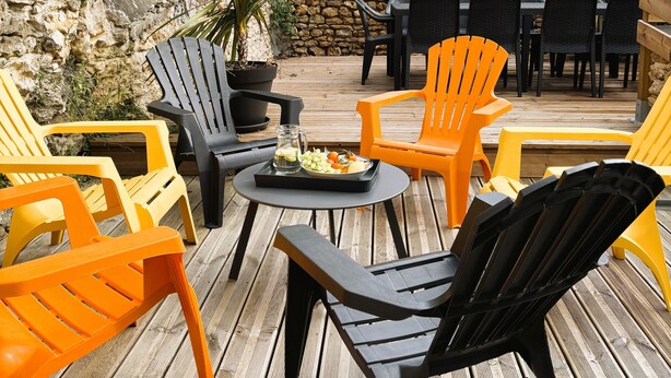 Un espace extérieur aménagé avec un sol en bois, des murs en pierre et un assortiment de chaises noires et orange.