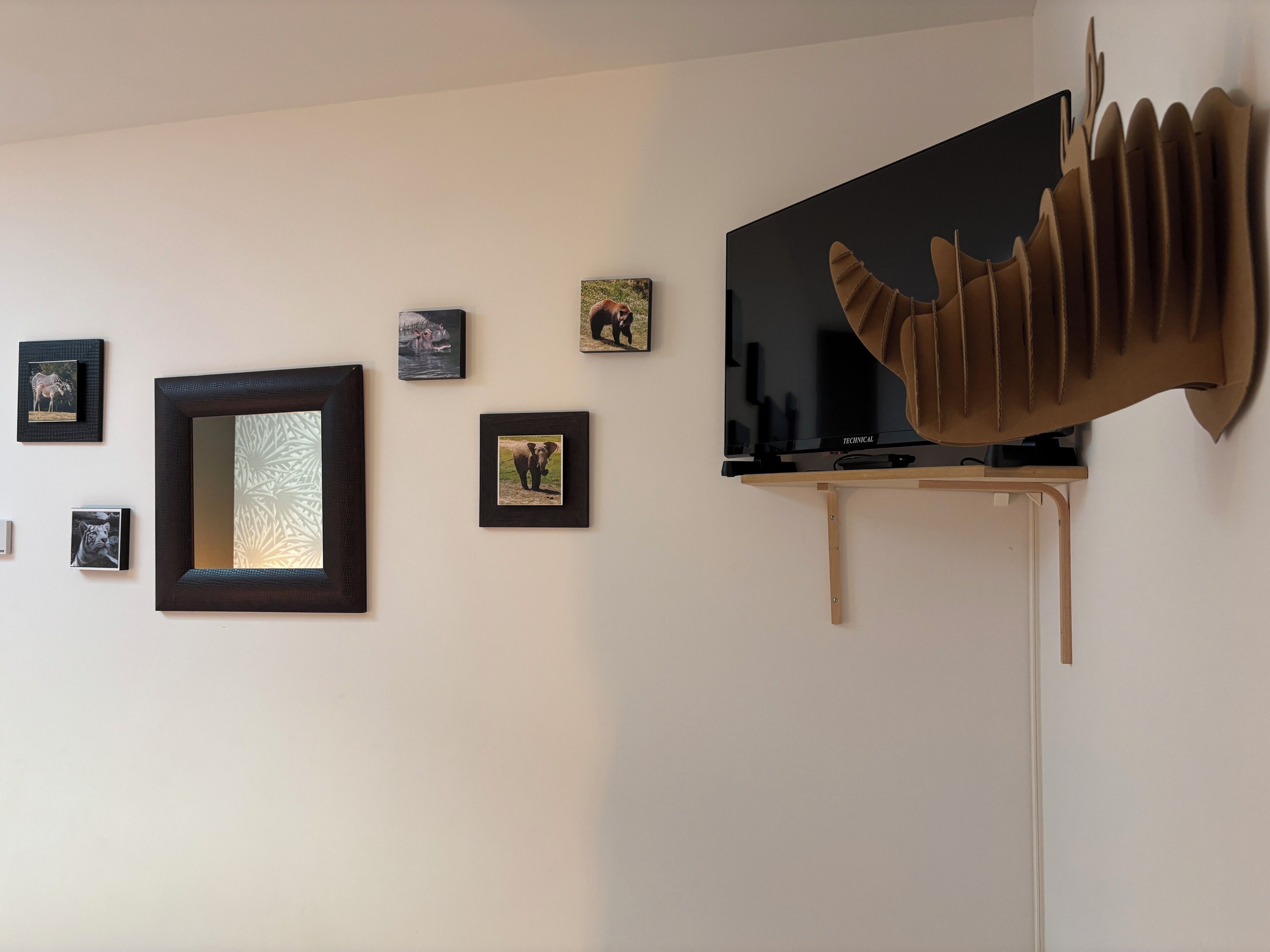 A wall with framed pictures, a mirror, and a mounted television.