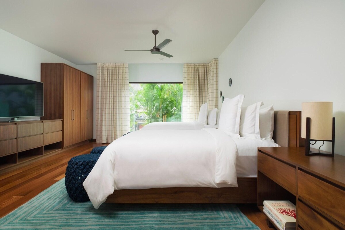 Ein Schlafzimmer mit Bett, Fernseher, Deckenventilator und Blick auf Grün.