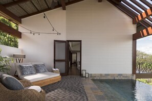 A bedroom with a bed, a nightstand, a lamp, a wicker chair, and a view of an outdoor swimming pool. - Four Seasons Resort Costa Rica At Peninsula Papaga (Nacascolo)