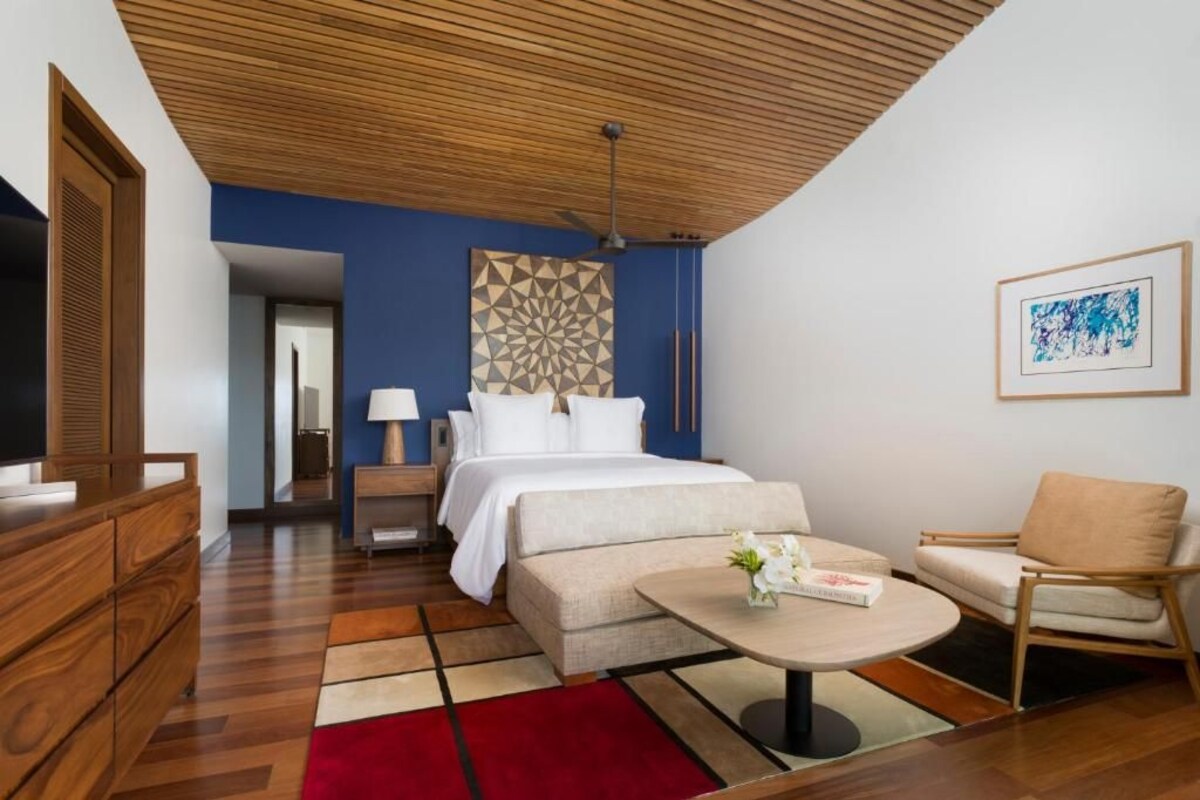 Ein Hotelzimmer mit einem Bett, einer Holzkommode, einem runden Couchtisch, einer Couch und einem Sessel.
