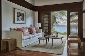 A living room with a sofa, a small table, a chair, a rug, and a window with blinds. - Four Seasons Resort Costa Rica At Peninsula Papaga (Nacascolo)