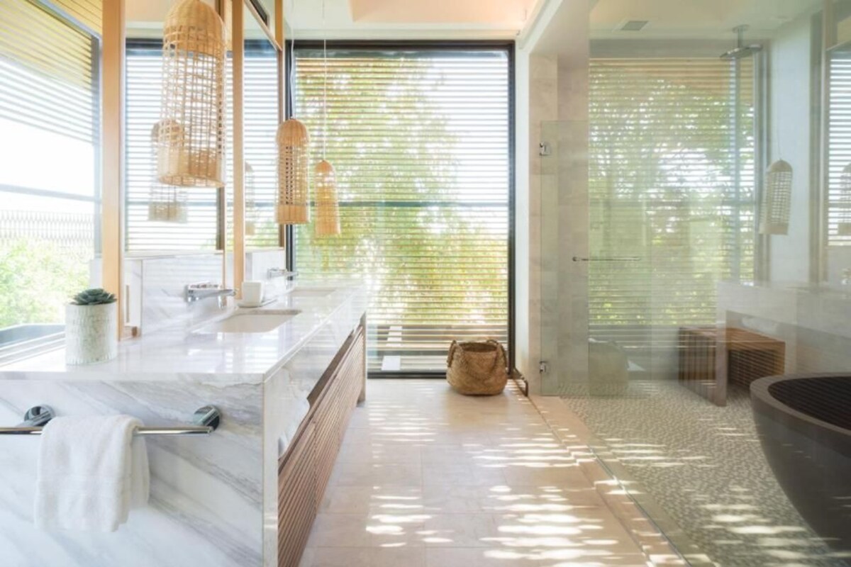 Ein modernes Badezimmer mit einer großen Badewanne, einer Duschkabine aus Glas und einem großen Fenster mit Jalousien.