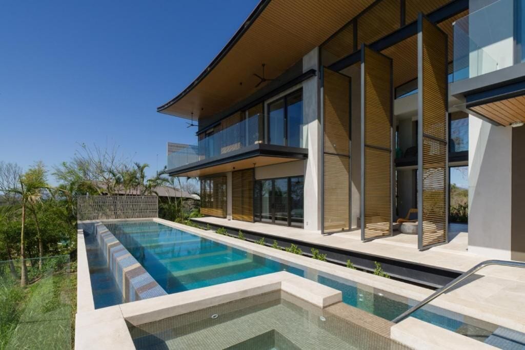 A modern two-story house with a swimming pool, large windows, and a balcony.