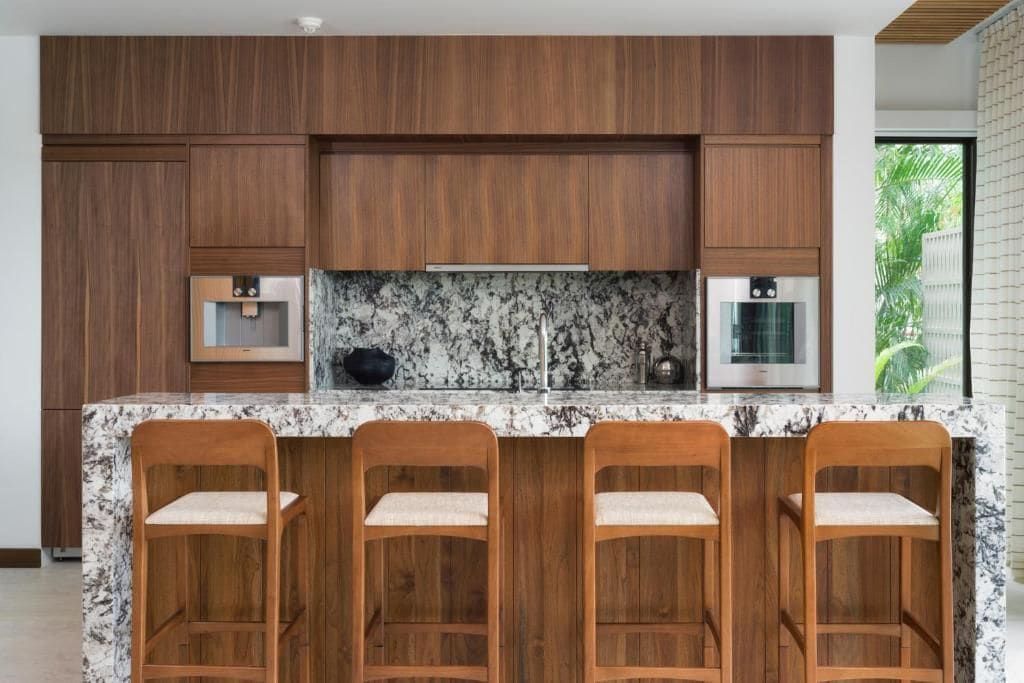 Una cocina moderna con armarios de madera, encimera de mármol y taburetes de bar.