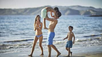A beach scene with a man lifting a child, a woman in a bikini, and a boy in swim trunks.