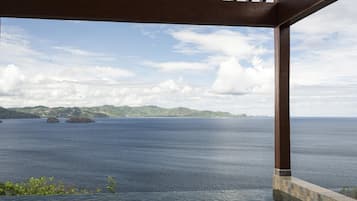 A view from a covered outdoor area with a pool, overlooking a calm sea and distant land.