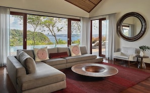Ein modernes Wohnzimmer mit einer großen Eckcouch, einem runden Couchtisch und Blick auf einen See und Hügel.