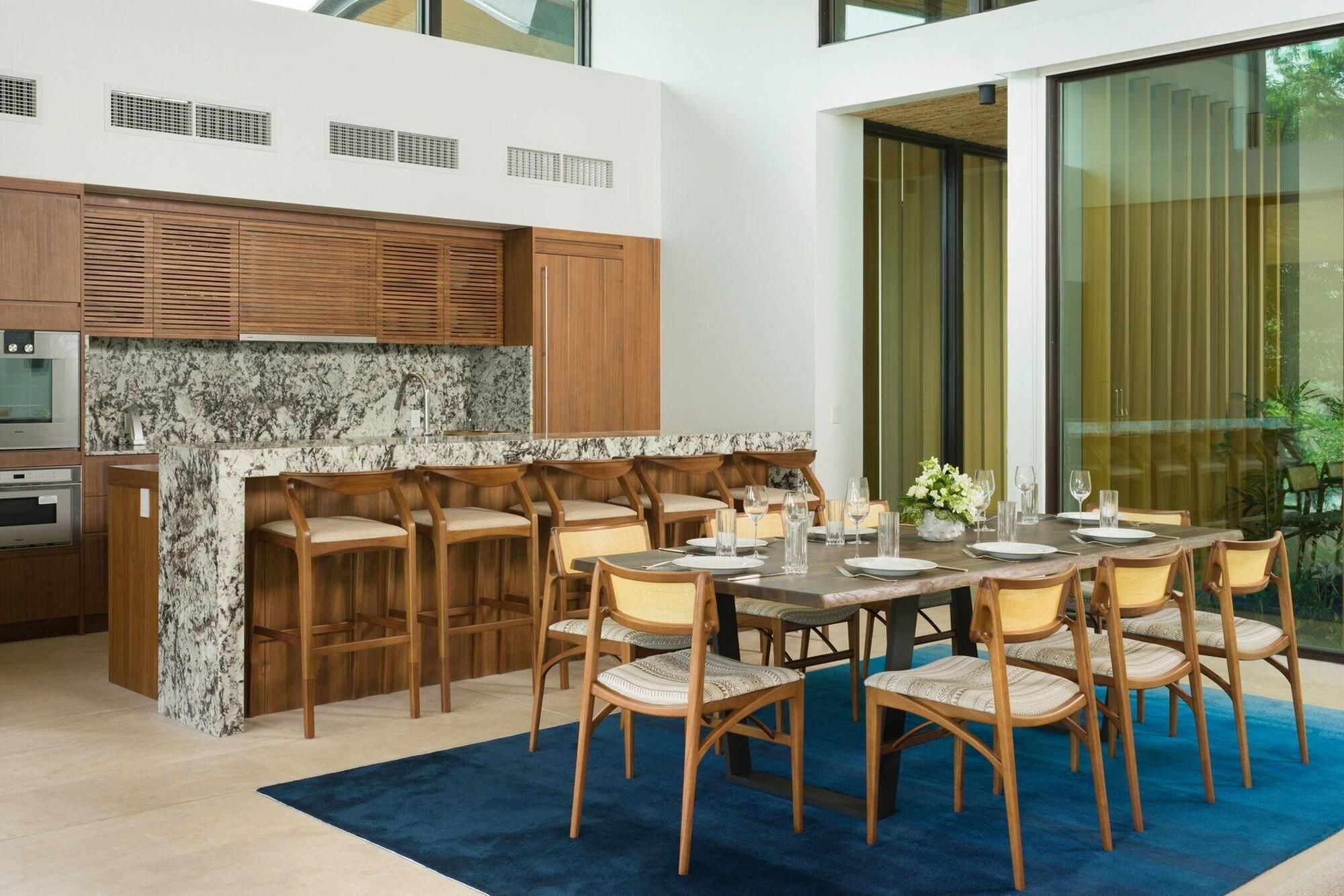 Une cuisine moderne avec des meubles en bois, un plan de travail en marbre et un coin repas comprenant des chaises en bois et un tapis bleu.