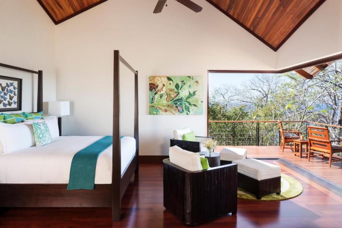 A bedroom with a bed, bedside table, and a view of an outdoor deck with seating.