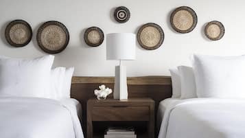 Quarto de hotel com duas camas, uma mesa de cabeceira com abajur e painéis de parede decorativos em tecido.