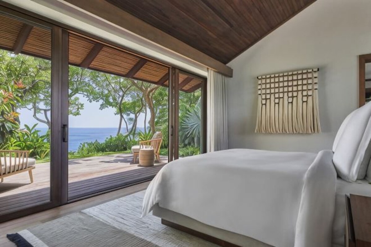 Un dormitorio con una cama grande, puertas de cristal correderas a un balcón y vistas al océano.