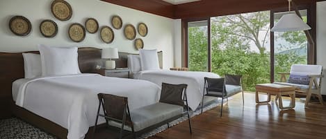 Habitación de hotel con dos camas, una zona de estar con sillas, una lámpara y vistas a zonas verdes.