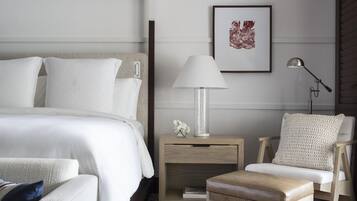 A hotel room with a bed, bedside table, lamp, chair, and a framed picture on the wall.