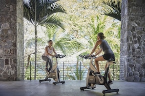 Two people exercising on stationary bikes in a room with stone walls and a view of greenery. - Four Seasons Resort Costa Rica At Peninsula Papaga (Nacascolo)