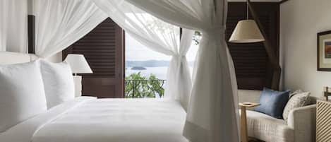 A bedroom with a bed, a nightstand, a lamp, a sofa, and a view of the outdoors.
