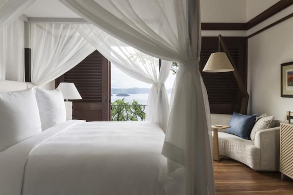 A bedroom with a bed, a nightstand, a lamp, a sofa, and a view of the outdoors. - Four Seasons Resort Costa Rica At Peninsula Papaga (Nacascolo)