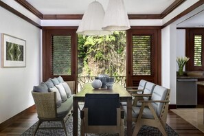 A dining area with a wooden table, two chairs, a sofa, and a view through large windows. - Four Seasons Resort Costa Rica At Peninsula Papaga (Nacascolo)