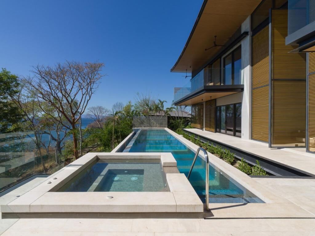 A modern pool area with clear water, a glass balustrade, and a view of the sea.