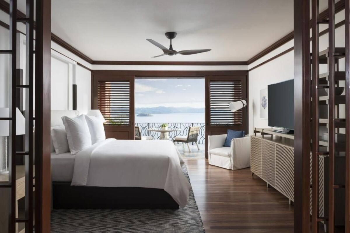 Ein Schlafzimmer mit Bett, Fernseher, einem Balkon mit Blick und Deckenventilator.