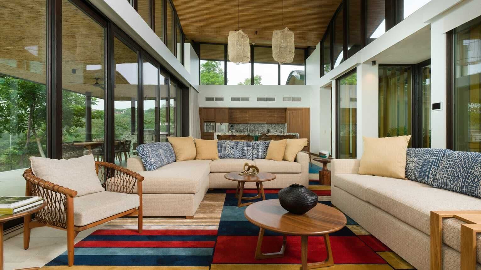 A modern interior with a sofa, armchair, and coffee table, large windows, and a kitchen area.
