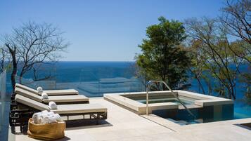 A rooftop infinity pool with a view of the ocean, lounge chairs, and a hot tub.