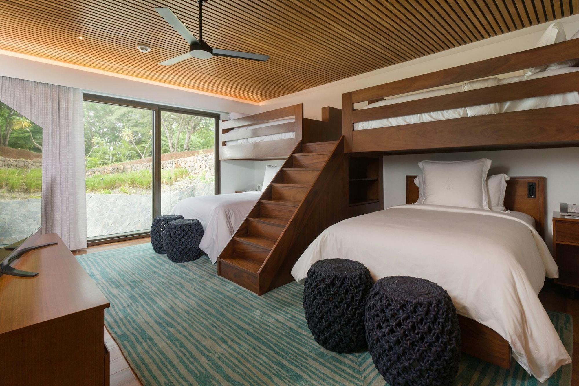 Un dormitorio moderno con techo de madera, literas, un escritorio y vistas a zonas verdes.