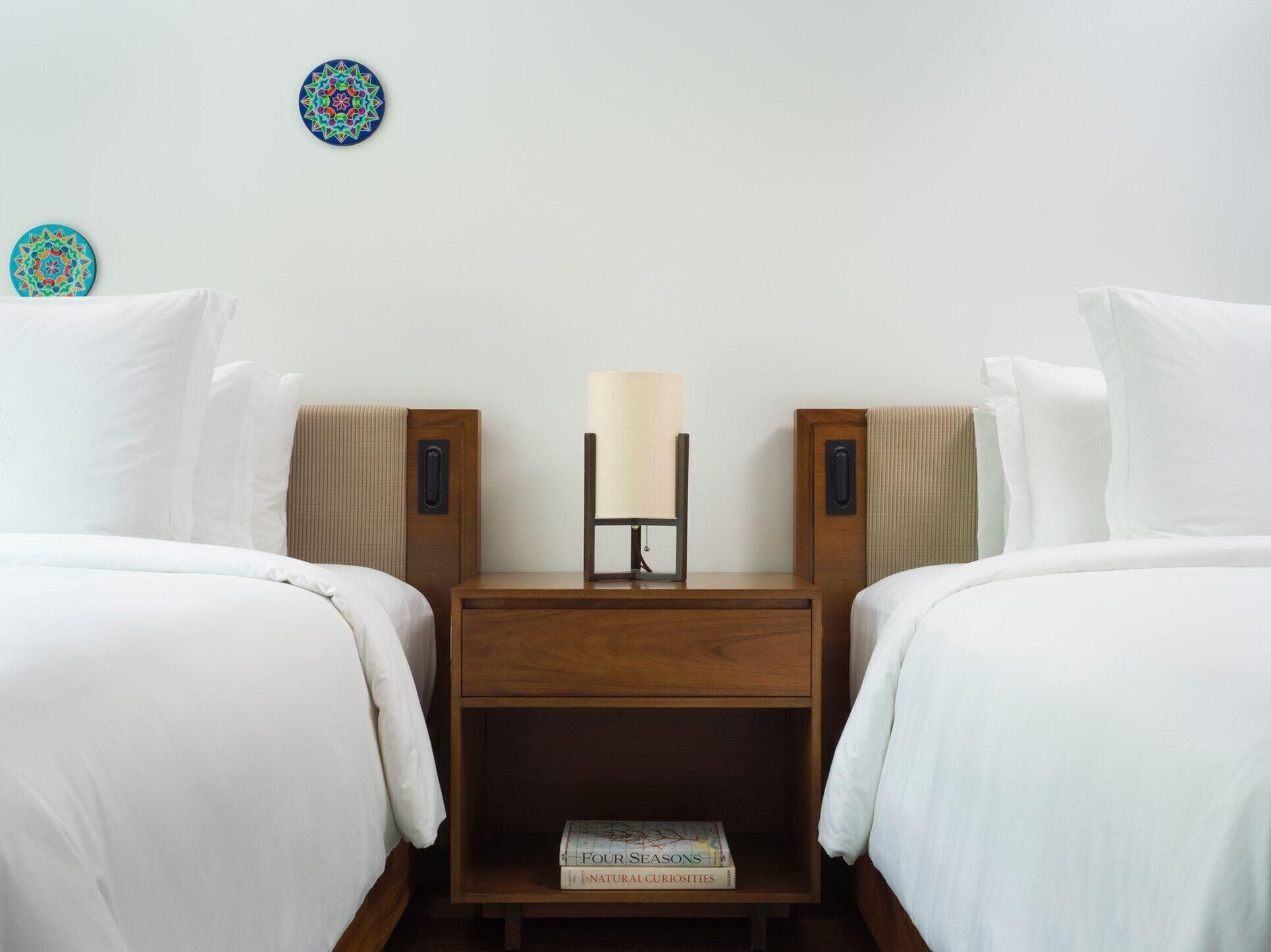 A hotel room with two beds, a nightstand, a lamp, and two decorative wall plates.