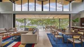 A spacious living area with a large sofa, dining table, and chairs, a view of greenery outside, and a high ceiling with natural light. - Four Seasons Resort Costa Rica At Peninsula Papaga (Nacascolo)
