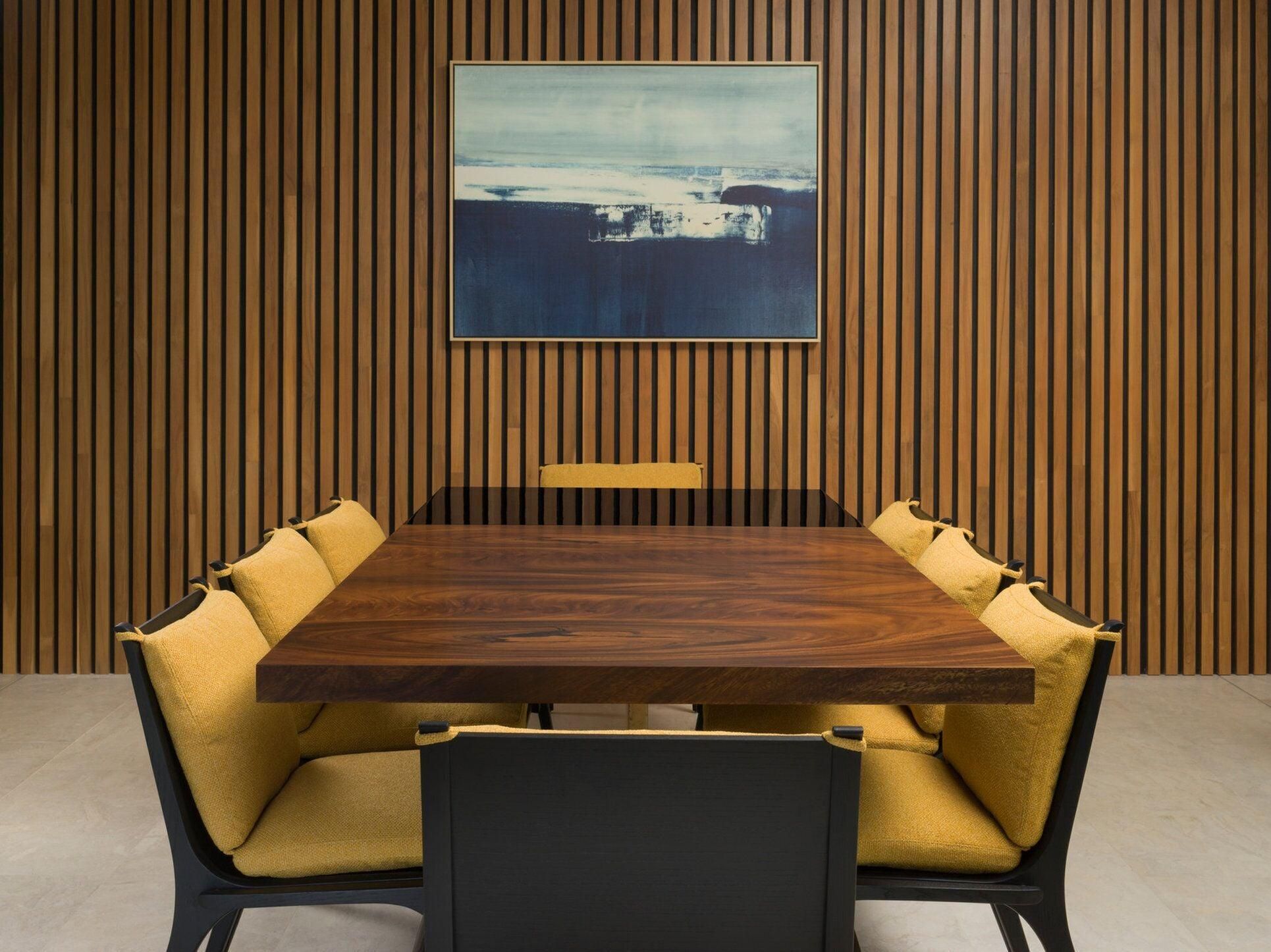 Un salón de conferencias con pared de paneles de madera, una mesa grande y sillas tapizadas en amarillo.