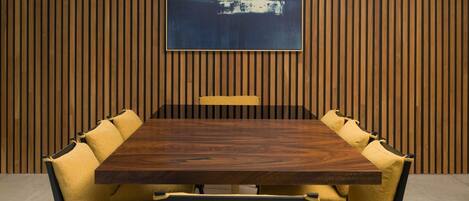Un salón de conferencias con pared de paneles de madera, una mesa grande y sillas tapizadas en amarillo.