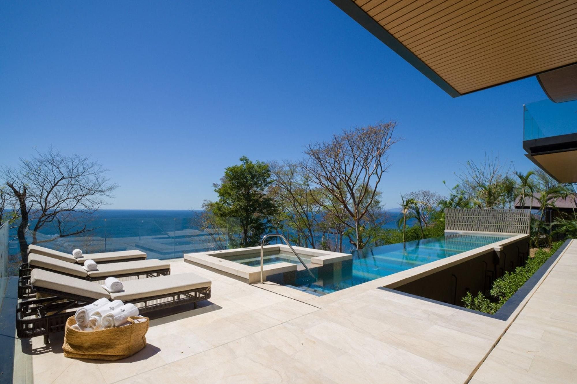 Uma área de piscina com espreguiçadeiras e vista para o mar.