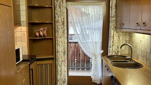 A kitchen with wooden cabinets, a built-in microwave, a sink, and a window with a view of a balcony. - Ciasa Nives (Badia)