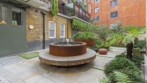 A courtyard with a circular wooden bench, a fire pit, and potted plants. - Westminster Fire Station Comfort Apartments (London)