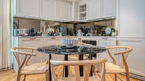 A modern kitchen with white cabinetry, a round dining table, and two wooden chairs. - Westminster Fire Station Comfort Apartments (London)