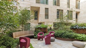 Un patio con zona de estar, macetas y un edificio con amplios ventanales.
