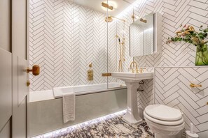 Ein modernes Badezimmer mit einer Wand im Fischgrätmuster, einer freistehenden Badewanne, einem Standwaschbecken und einer Toilette.