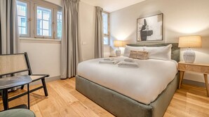 Habitación de hotel con una cama grande, dos lámparas de noche, una silla y una ventana con cortinas.
