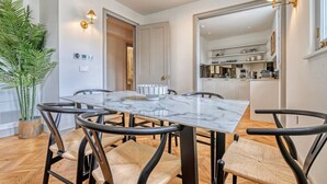 Un moderno comedor con una mesa de mármol y sillas negras, una planta en maceta, y una cocina al fondo.